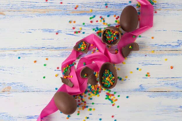 Uova di cioccolato pasquali, nastro rosa, dolci multicolori sulla vecchia superficie di legno bianca. Concetto di pasqua