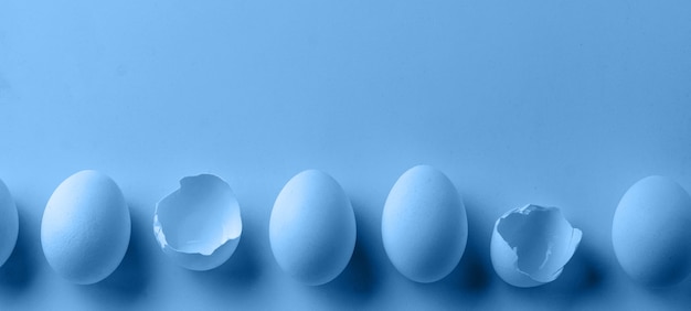 Uova di gallina crude bianche che si trovano in fila orizzontale con uovo rotto, vista dall'alto.