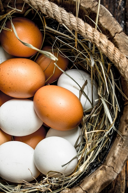 Uova di gallina fresche in un vecchio secchio di legno. Su uno sfondo di legno.