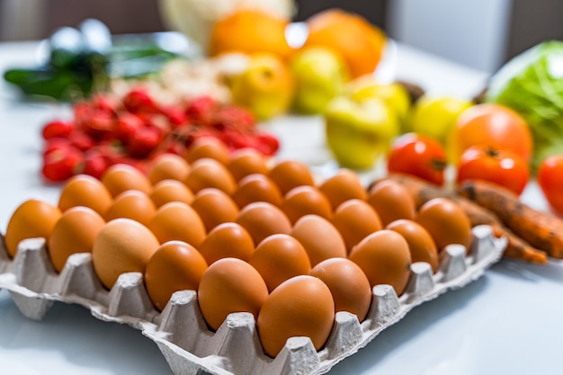 Uova di gallina in scatola di cartone sul tavolo. Frutta e verdura fresche sfocate sullo sfondo. Concetto di cibo rustico.