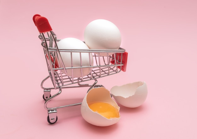 Uova di gallina in un mini carrello della spesa su una superficie rosa. Avvicinamento.