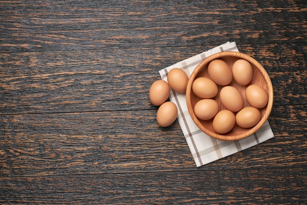 Uova di gallina in una ciotola di legno su un tavolo da cucina, vista dall'alto.