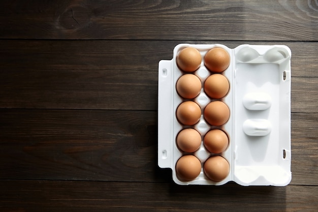 Uova di gallina in una scatola bianca su un tavolo di legno marrone