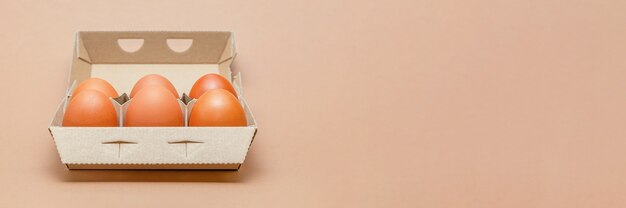 Uova di gallina in una scatola di cartone, spazio per il testo, ampio formato. Sfondo marrone.