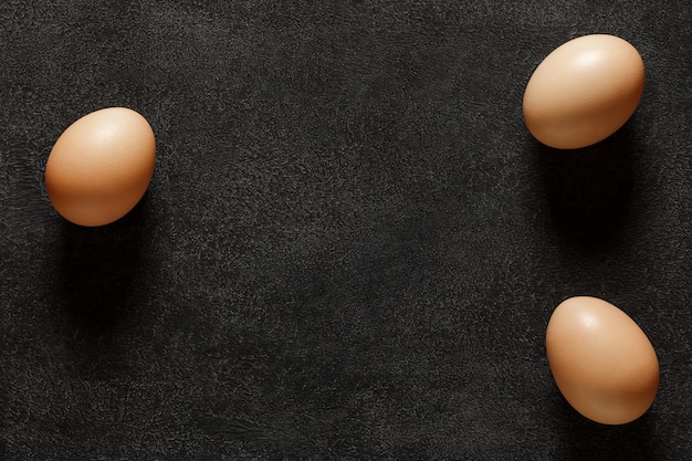 Uova di gallina intere tre pezzi su sfondo scuro vista dall'alto spazio per copiare il testo