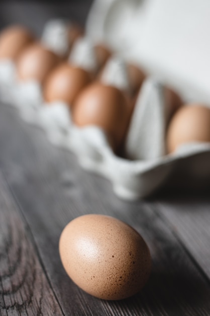 Uova di gallina marrone in un cartone su superficie di legno.