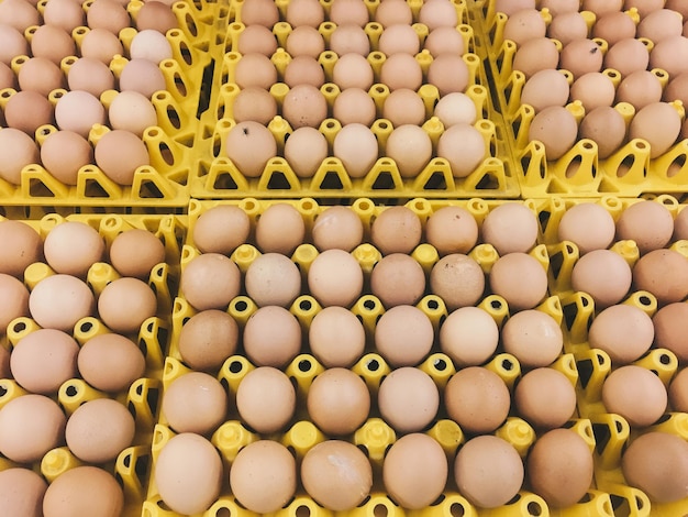 Uova di gallina marroni o crude nel cartone giallo del vassoio delle uova con spazio per le uova impilano l'uovo sulla scatola