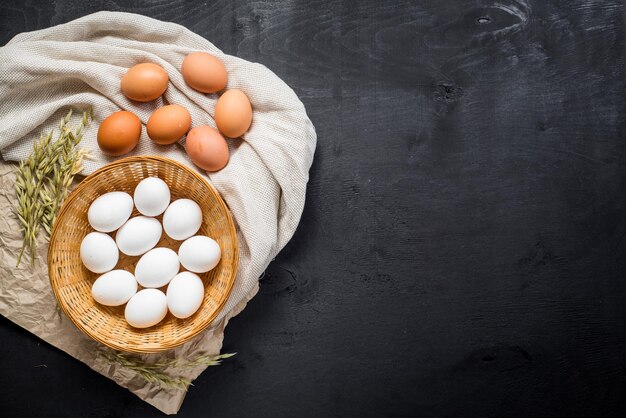 Uova di gallina nel cestino su fondo di legno nero. Copia spazio