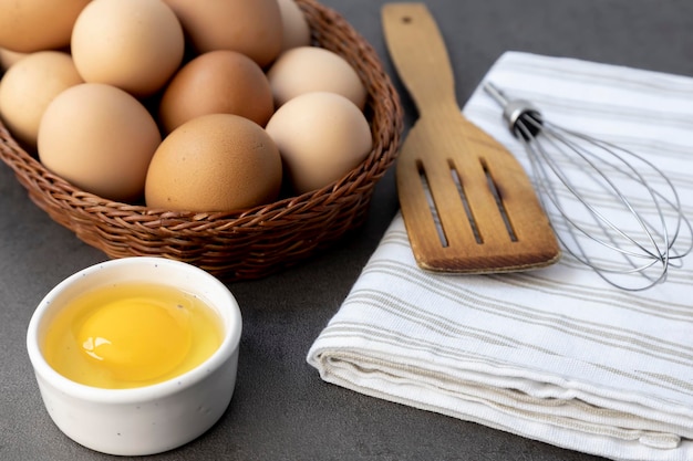 Uova di gallina ruspanti in un cesto di vimini Uovo rotto tuorlo d'uovo Una spatola di legno e una frusta