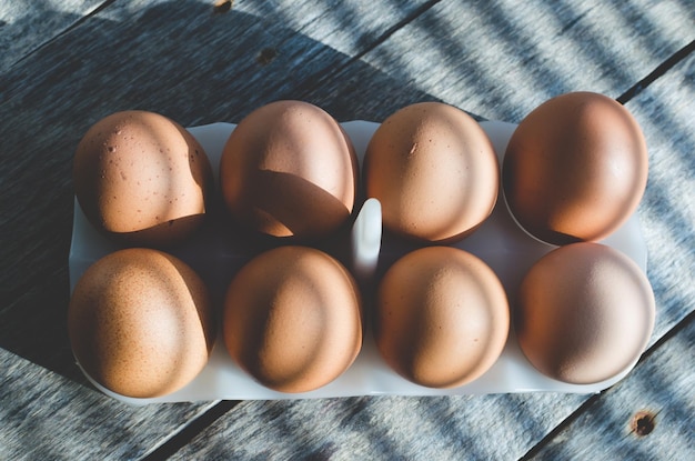 Uova di gallina su un vecchio tavolo di legno al primo sole Le ombre delle persiane cadono sullo sfondo e le uova