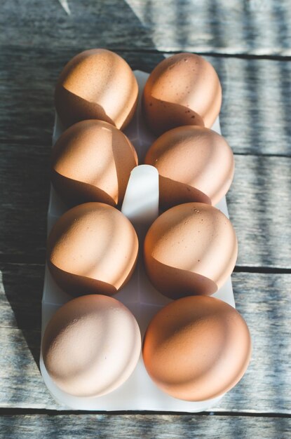 Uova di gallina su un vecchio tavolo di legno al primo sole Le ombre delle persiane cadono sullo sfondo e le uova