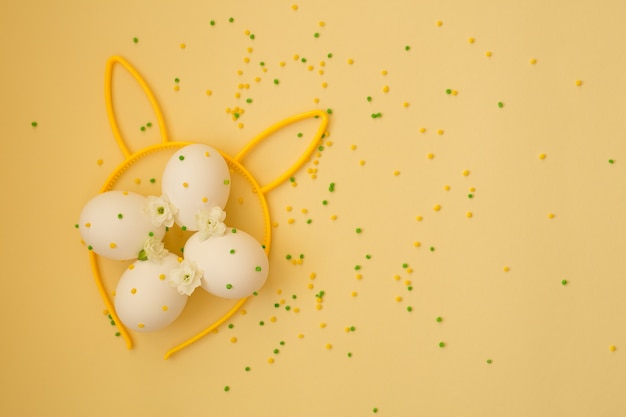 Uova di Pasqua bianche con pois su sfondo giallo con orecchie da coniglio.