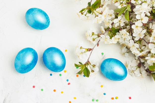 Uova di Pasqua blu viola, fiori di primavera mela, ciliegia, caramelle colorate su uno sfondo di pietra bianca