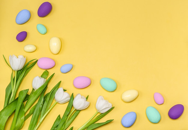 Uova di Pasqua colorate con un mazzo di tulipani bianchi su sfondo giallo, copia spazio,