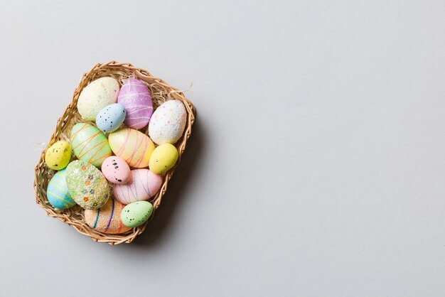 Uova di Pasqua colorate in cesto di vimini su sfondo colorato primo piano vista dall'alto con spazio di copia
