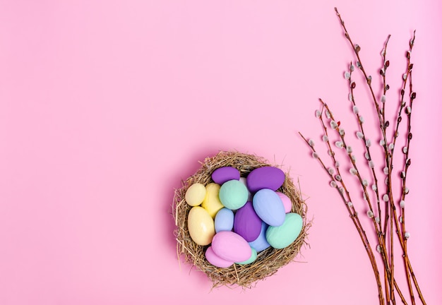 Uova di Pasqua colorate in un nido decorativo di rami di paglia e salice su uno sfondo rosa, copia spazio, piatto laici