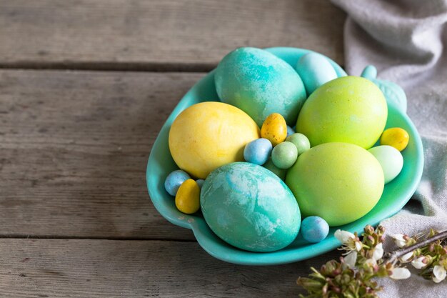 uova di Pasqua colorate in un piatto turchese su uno sfondo di legno squallido