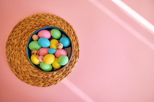 Uova di Pasqua colorate in una ciotola, sfondo rosa, vista dall'alto