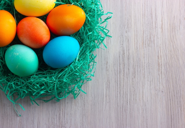 Uova di Pasqua colorate nel nido verde sul legno bianco.