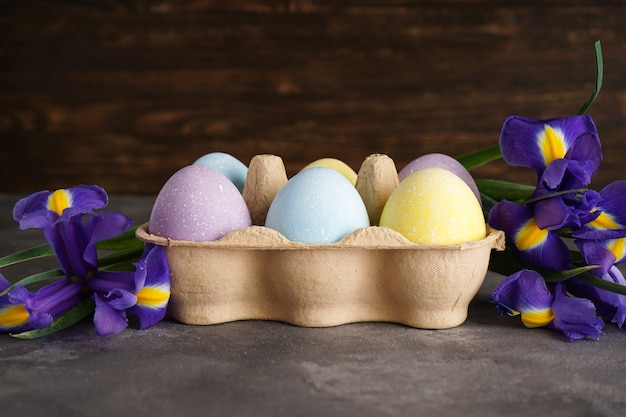 Uova di Pasqua colorate pastello in una scatola di cartone e fiori freschi su uno sfondo di legno.