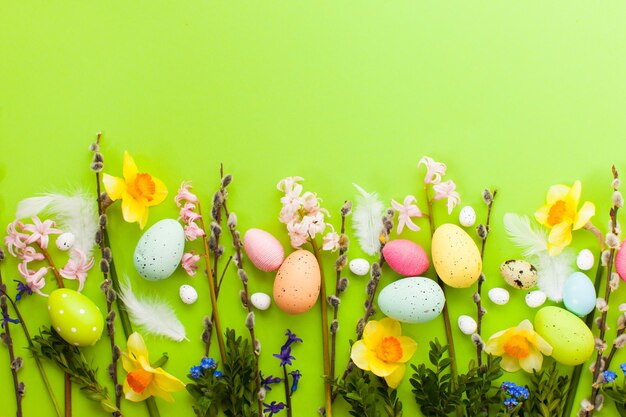 Uova di Pasqua con fiori spting e rami di salice su sfondo verde vivido. Vista dall'alto, posto per il testo - auguri per le vacanze