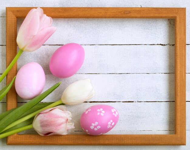 Uova di Pasqua, cornice per foto, tulipani su un fondo di legno bianco.