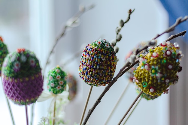 Uova di Pasqua decorate con perline di colore brillante con ramo di un albero di vimini su sfondo bianco sfocato