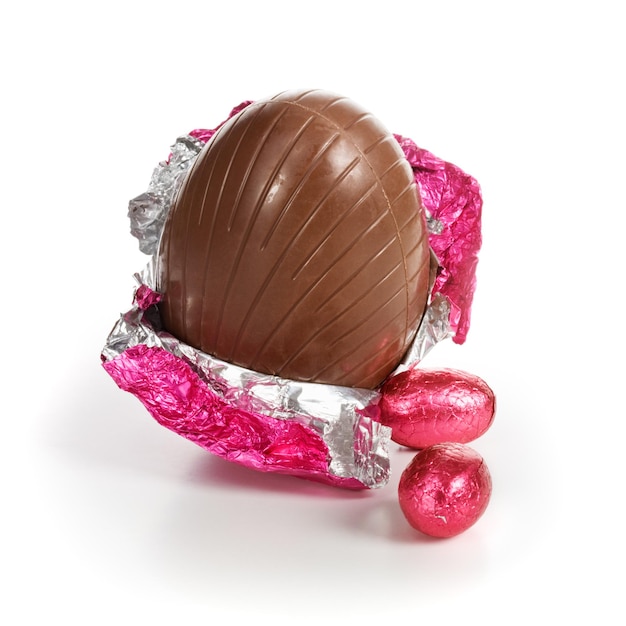 Uova di Pasqua di caramelle al cioccolato avvolte in un foglio rosa su sfondo bianco