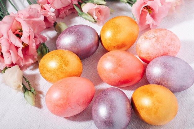 Uova di Pasqua dipinte di viola e rosa oro in colori pastello e fiori su una tovaglia di cotone bianco