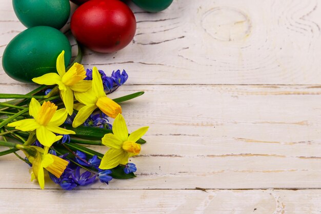 Uova di Pasqua dipinte e bouquet di narcisi gialli e fiori di scilla blu su sfondo di legno bianco Composizione pasquale Vista dall'alto copia spazio