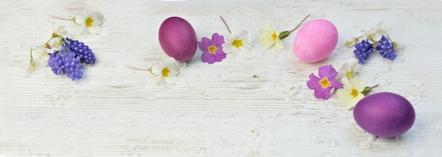 Uova di Pasqua dipinte in rosa e viola su un tavolo tra fiori e petali primaverili