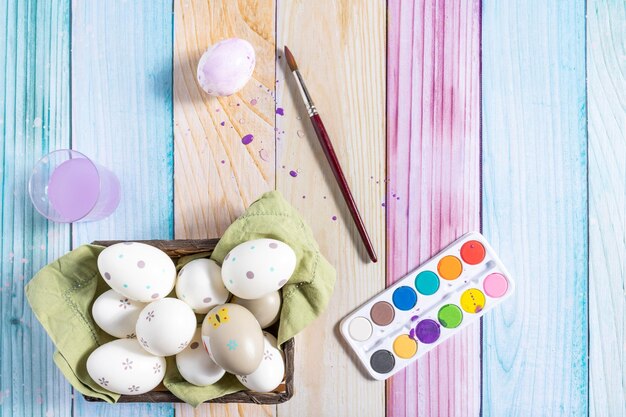 Uova di Pasqua dipinte in un cestino ed elementi da dipingere su uno sfondo di legno colorato