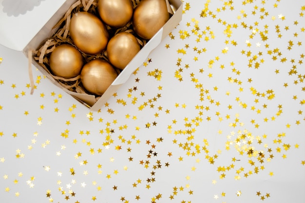 Uova di Pasqua dorate in una scatola con le stelle dorate su fondo bianco