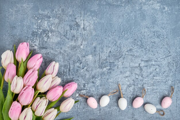 Uova di Pasqua e tulipani rosa sul muro grigio.