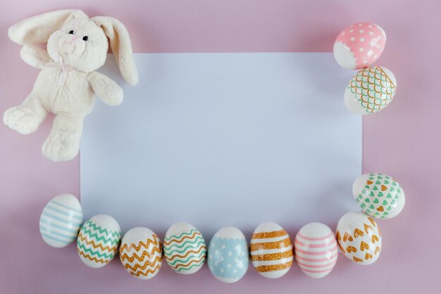 Uova di Pasqua in colori pastello con motivo e coniglio giocattolo bianco su sfondo pinkblue
