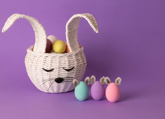 Uova di Pasqua in un cestino a forma di coniglietto di Pasqua Decorazioni festive su sfondo viola