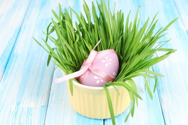 Uova di Pasqua in una ciotola con erba sulla tavola di legno blu da vicino