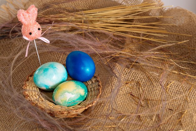 Uova di Pasqua multicolori di toni blu e due coniglietti pasquali su un bastone su uno sfondo di stoffa