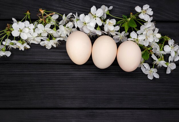 Uova di Pasqua naturali con fiori primaverili bianchi su fondo in legno