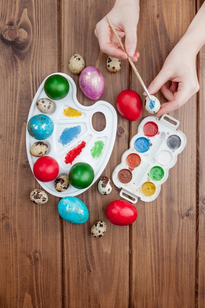 Uova di Pasqua, pitture e spazzole dipinte a mano su fondo di legno. Preparazione per le vacanze. Le mani delle ragazze disegnano un motivo