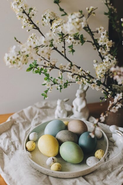 Uova di Pasqua su piatto con figurine di coniglietto tovagliolo di lino fiori di ciliegio su tavola rustica