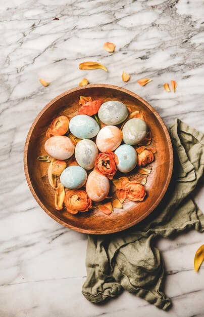 Uova di Pasqua tinte e petali di fiori in fiore in piatto di legno