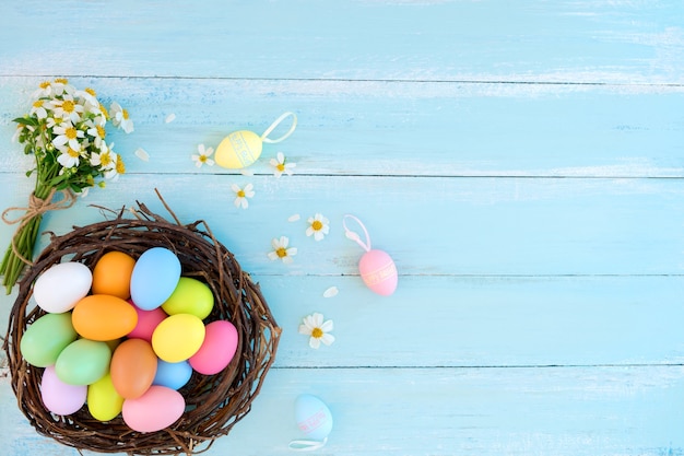 Uova di Pasqua variopinte in nido con i wildflowers sopra sul fondo di legno rustico delle plance