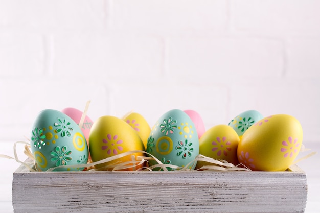 Uova di Pasqua variopinte in scatola di legno su fondo bianco. Sfondo vacanze di Pasqua. Copia spazio