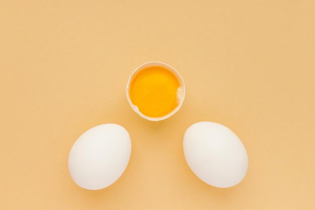 Uova di pollo bianche intere e metà incrinate al centro con tuorlo crudo su sfondo giallo Minimalismo Vista dall'alto
