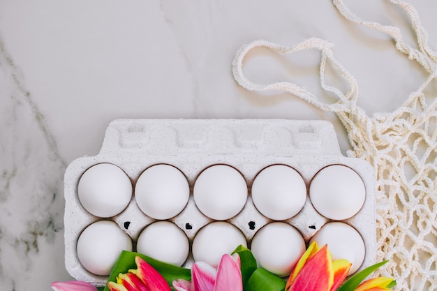 Uova di pollo piatto e tulipani colorati, borsa eco su fondo di marmo