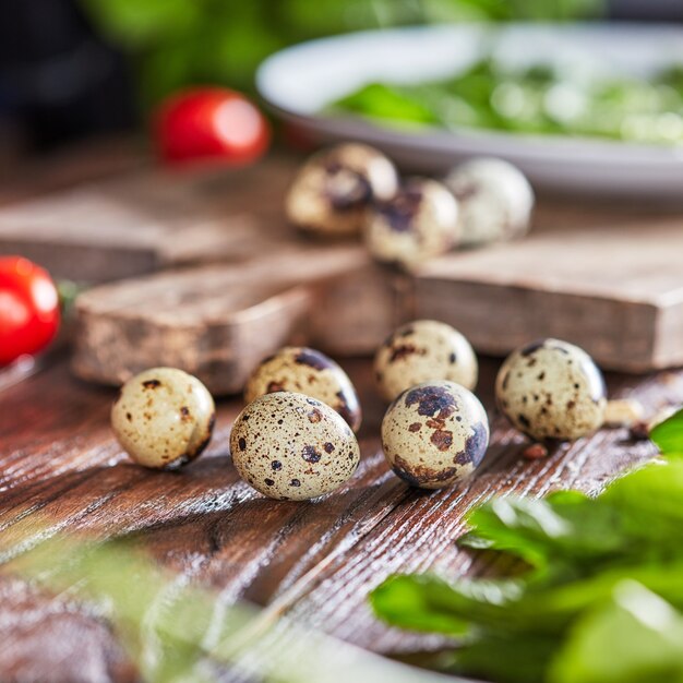 Uova di quaglia organiche su un vecchio tavolo da cucina in legno con pomodori e verdure fresche. Cibo salutare