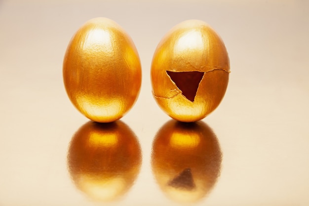 Uova dorate intere e incrinate poste su un tavolo riflettente