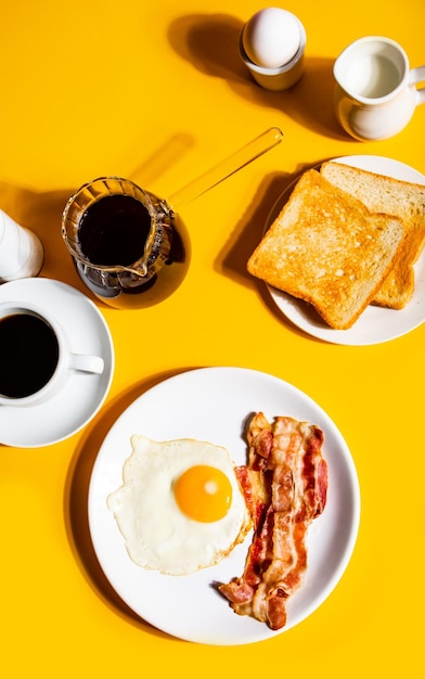 uova fritte con pancetta arrostita caffè nero pane tostato su sfondo giallo colazione retrò americana