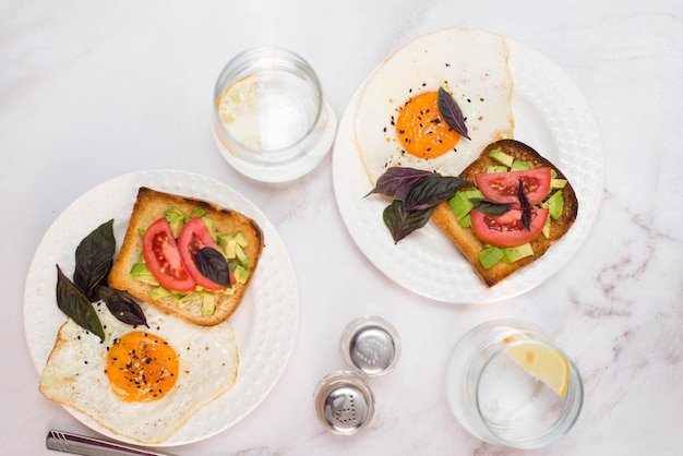 uova fritte con panini con avocado, pomodoro e bicchiere d'acqua